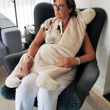 Voksen sidder med Koko Nora vægttæppe formet som dyr i stol – beroligende og sansestimulerende tyngdetæppe

