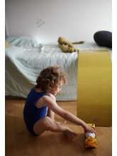 Barn sidder på gulvet ved kinderfeets balancebræt i farven mustard , der er sat op på seng som rutchebane.