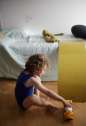 Barn sidder på gulvet ved kinderfeets balancebræt i farven mustard , der er sat op på seng som rutchebane.