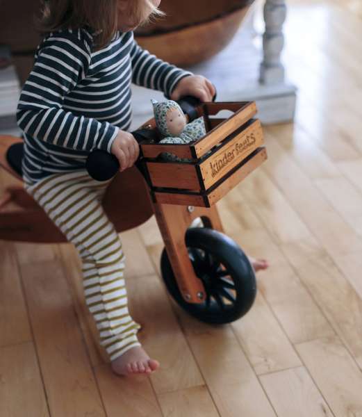 Barn kører på kinderfeets cykel med kasse på. Der er en dukke i kassen.