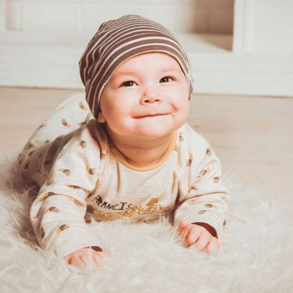 Baby ligger på maven og smiler på blødt tæppe – sanseprofil infant 0-6 måneder – vicca.dk

