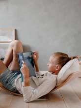 Teenage pige ligger på Kinderfeets Kinderboard Large, natural og læser