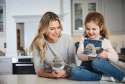 Warmies næbdyr sider på et køkkenbord, sammen med en pige og hende mor 