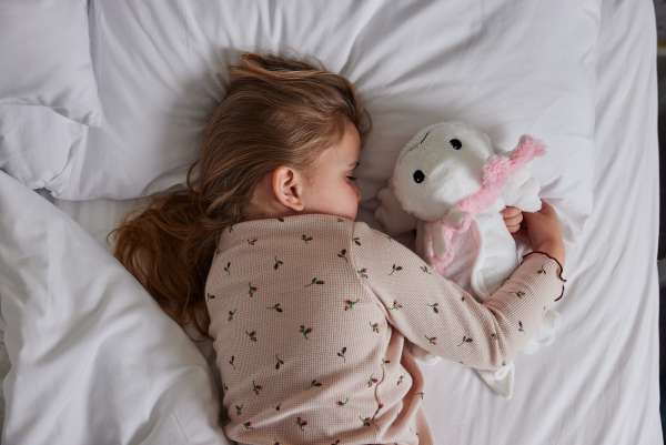 Sansebamse Warmies Axolotl sover sammen med en pige i en seng 