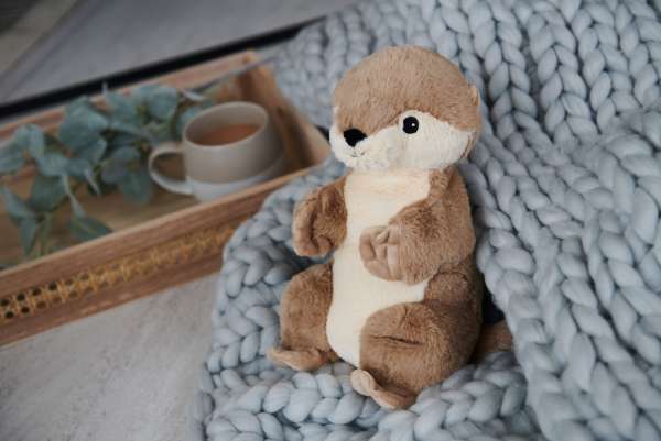 Sansebamse Warmies odder på tæppe ved sofabord – blød bamse til ro, hygge og sansestimulering


