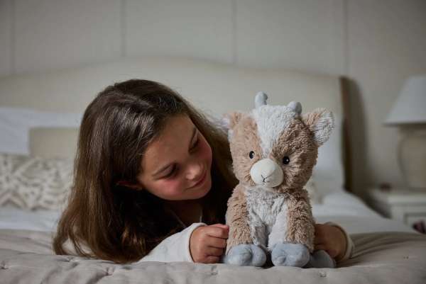 En pige ligge i en seng sammen med Sansebamse Warmies siddende ged