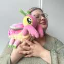 Person holder Orchidé-knæler plush bamse tæt ved kinden – pink kawaii insekt med blødt design i brug

