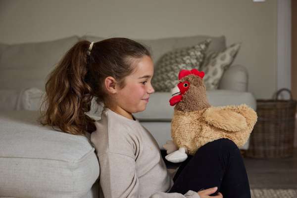Sansebamse Warmies® brun høne og en pige sidder på gulvet foran en sofa