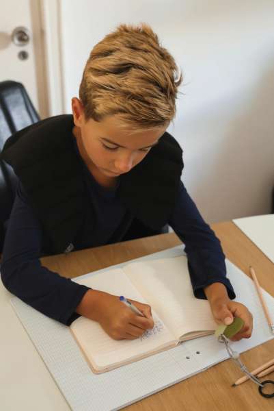 En dreng sidder ved et bord og skriver CalmCircle 2-i-1 fidget og bideredskab