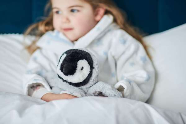 Sansebamse Warmies® baby pingvin sidder sammen med en pige 