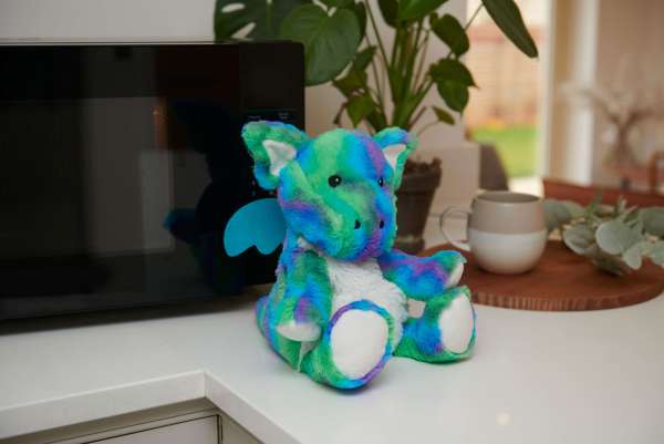 Sansebamse Warmies® regnbuedrage sider på et bord