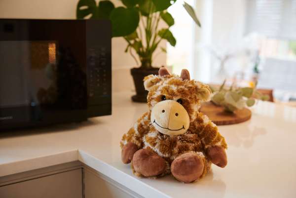 Sansebamse Warmies® giraf sidder på et bord 