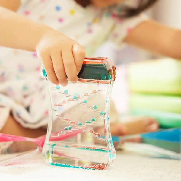 Barn leger med zig-zag sanse timeglas hvor små kugler bevæger sig gennem banen i væsken



