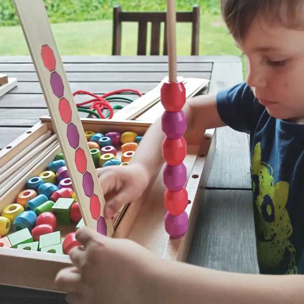 dreng lege med Andreu Toys tråde- og stablespil – robuste træbrikker og kreative mønstre.

