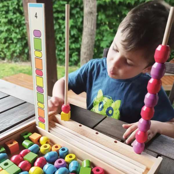 Andreu Toys tråde- og stablespil – kreativt læringslegetøj til finmotorik. stå på et borg imens en dreng lege med det 

