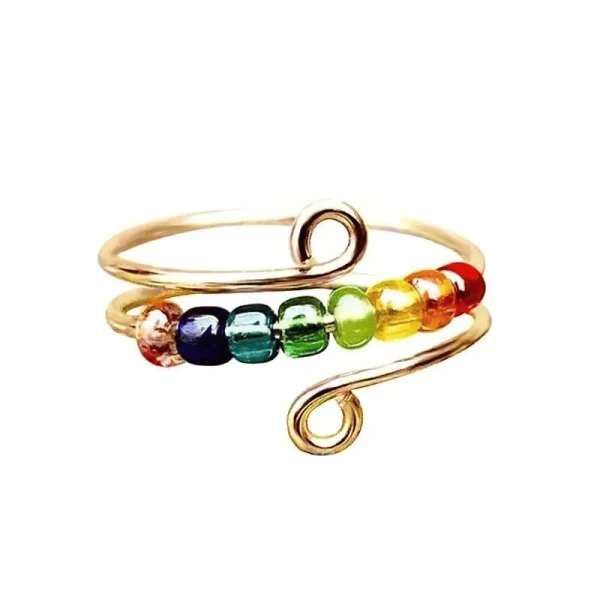 Guldfarvet Bifrost fidgetring med otte regnbuefarvede bevægelige glasperler – elegant fidgetsmykke til uro i hænderne, fokus og afslapning.

